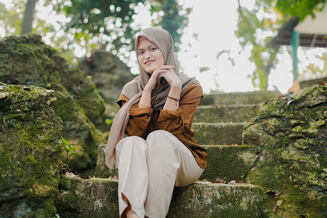 portrait, muslim, smiling, hijab, stone steps, moss, nature, outdoors, greenery, brown, white, beige, modern clothing, landscape, style, outdoor portrait, femininity, outdoor setting, comfort