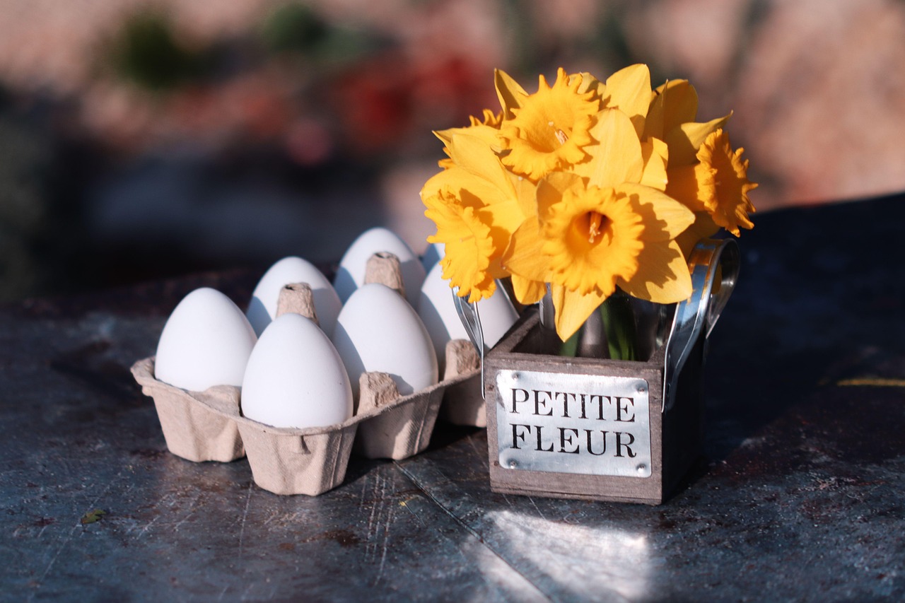 spring still life, yellow daffodils, easter decoration, white eggs, rustic table, flower bouquet, fresh flowers, easter theme, springtime vibes, petite fleur, country style, floral centerpiece, egg carton, seasonal decor, easter morning, nature beauty, floral art, blooming flowers, holiday arrangement, spring celebration, cheerful scene, pastel flowers, daffodil bouquet, symbolic rebirth, farm to table